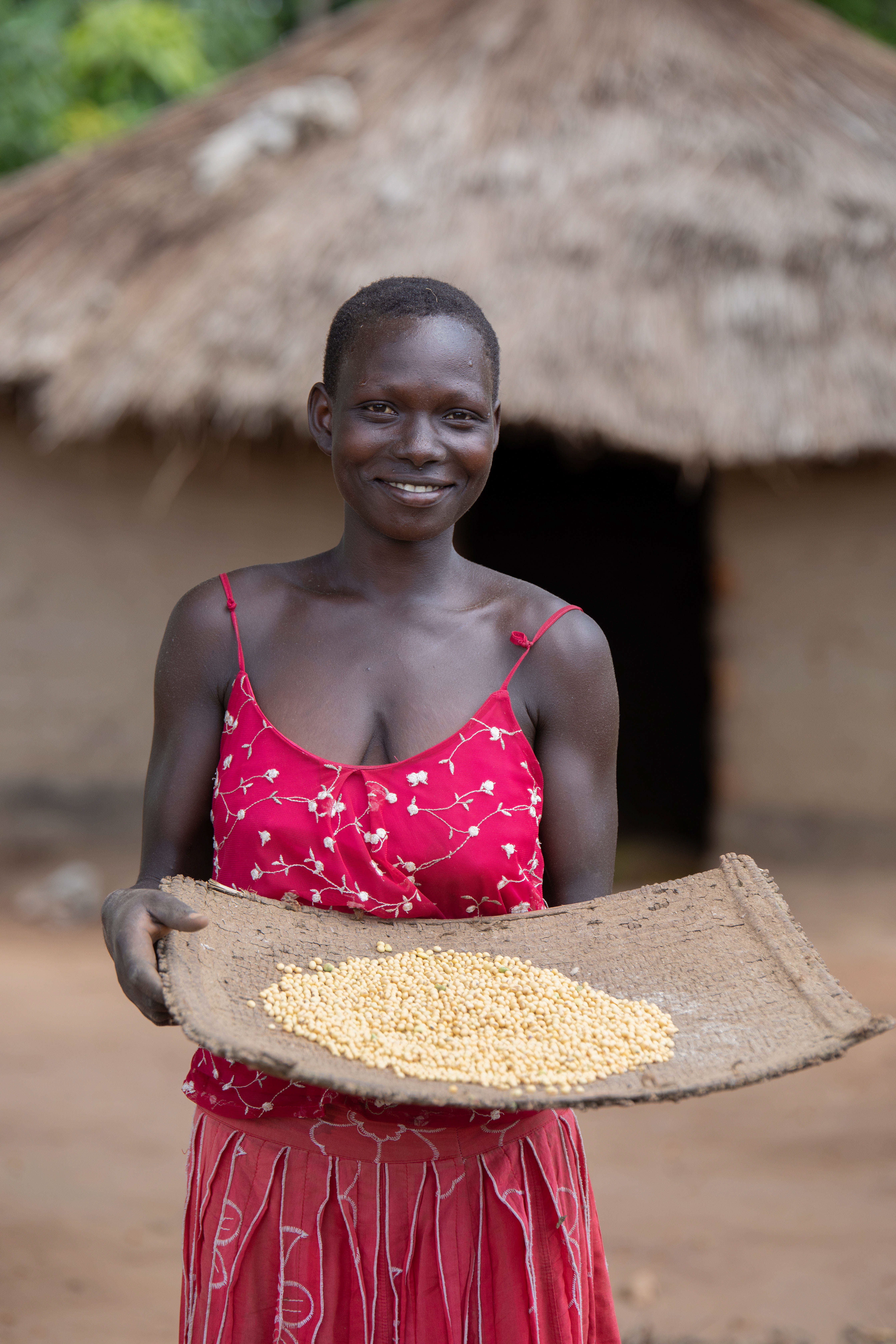 A woman poses with a tray of soybean seeds in Uganda.