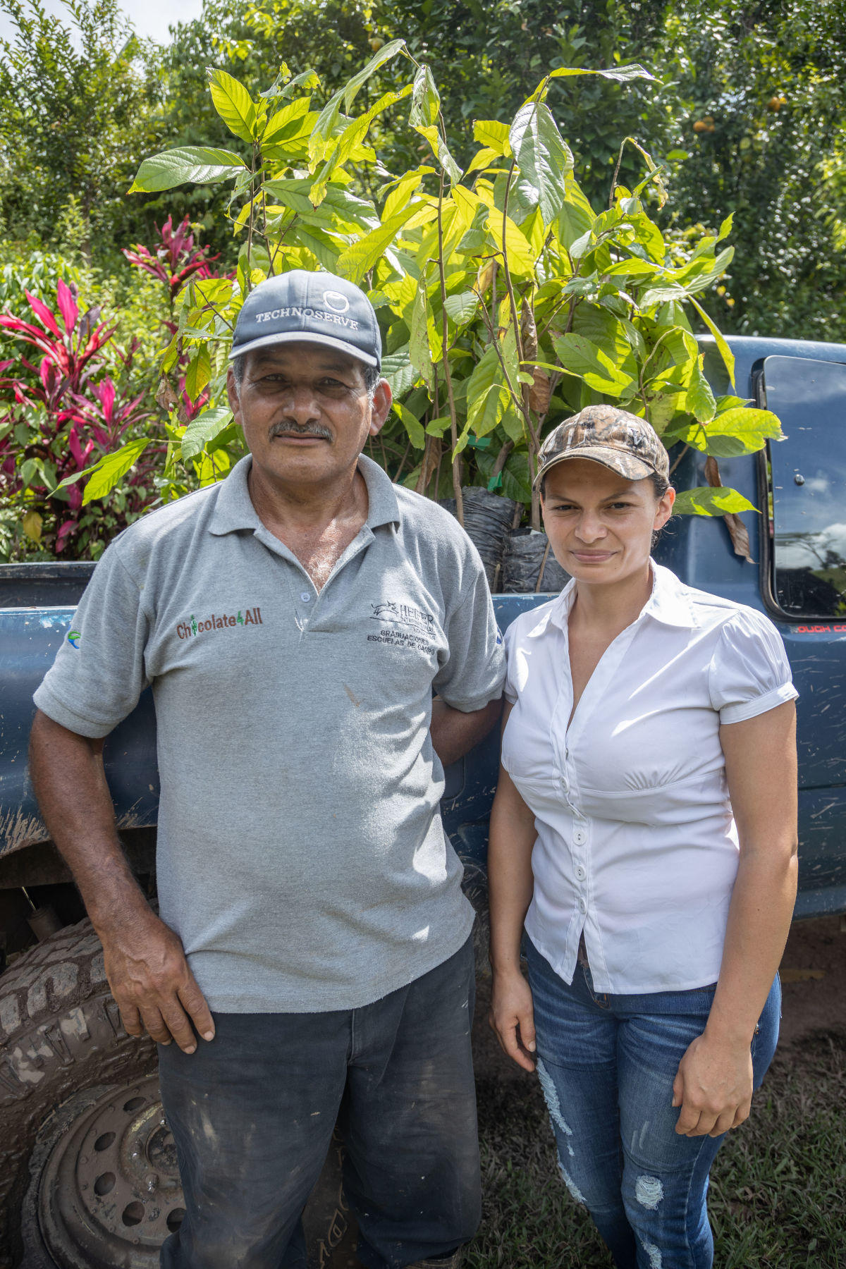A young woman and a man standing in front of a truck of cacao plants they grow in their farm. 