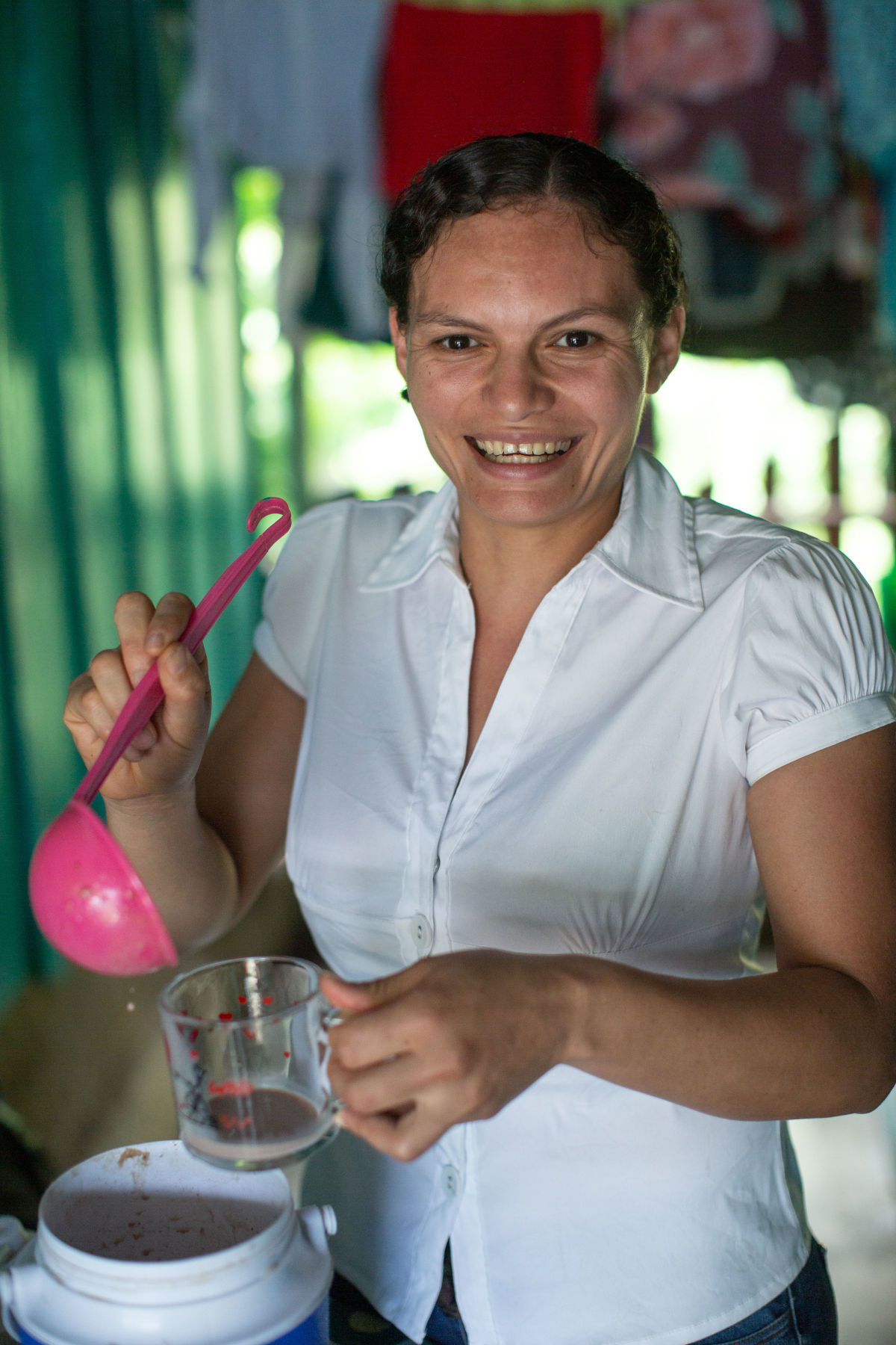 A young woman in a white attire pouring hot chocolate in a cup.