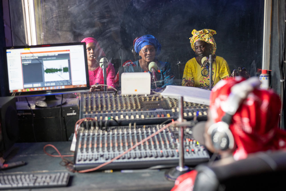 Three women speak into microphones in a radio recording station.