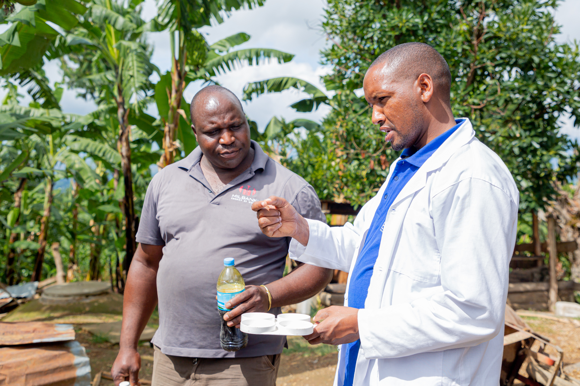 A young man wearing a white lab coat talking to a man standing beside him.