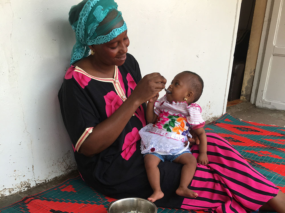 A woman feeds her baby porridge from a bowl.