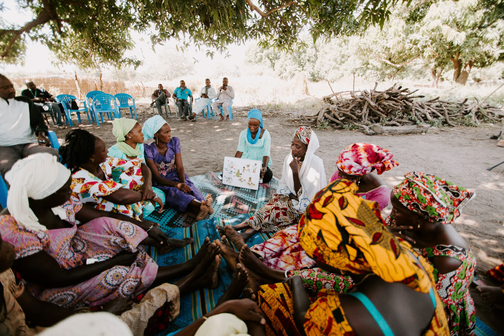 Women sitting on the ground and watching a presentation about nutrition.