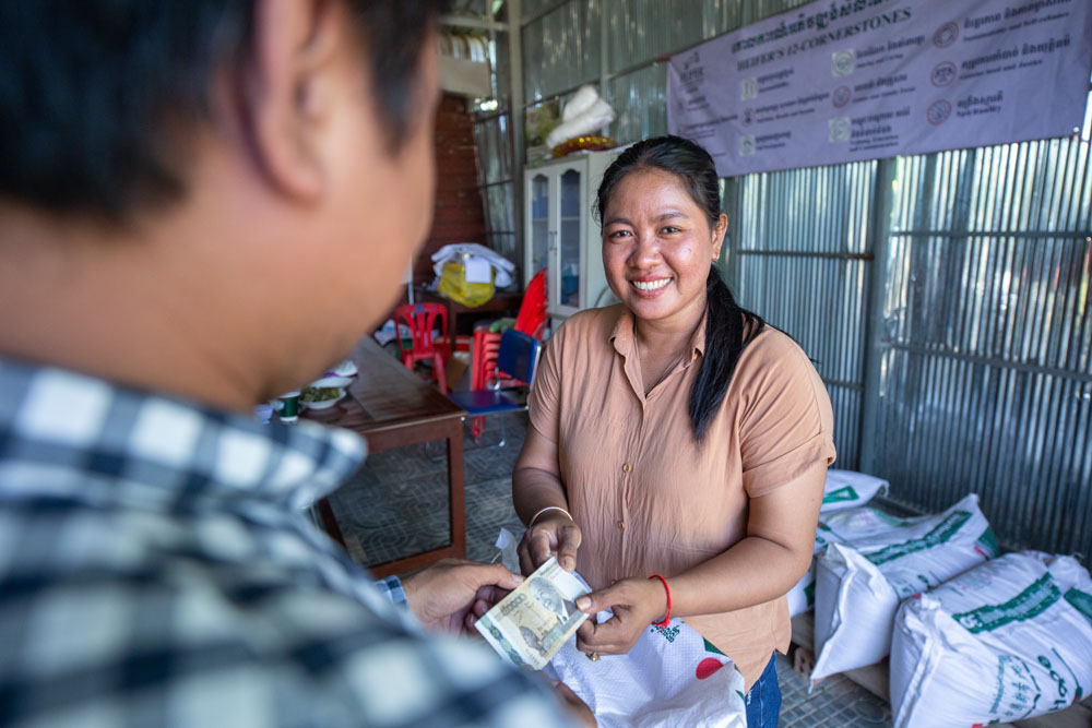 Set Hach exchanges paper bills with a customer in her store while weighing a bag of animal feed.