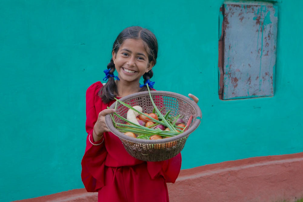 A young girl holds a basket of fresh produce in Belbari, Nepal.