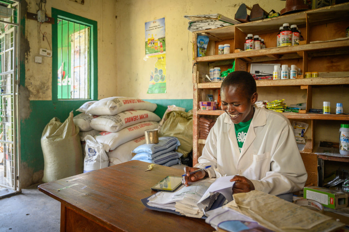 A woman studies a financial record book while sitting in her shop where she sells seeds, fertilizers and health care products for livestock and poultry.