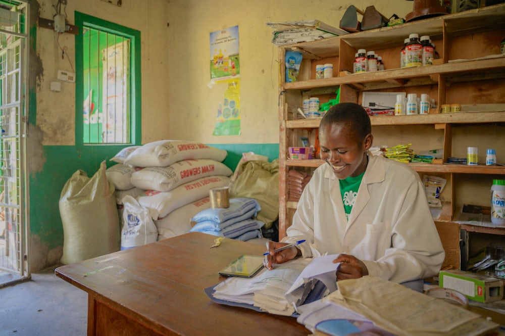 A woman studies a financial record book while sitting in her shop where she sells seeds, fertilizers and health care products for livestock and poultry.