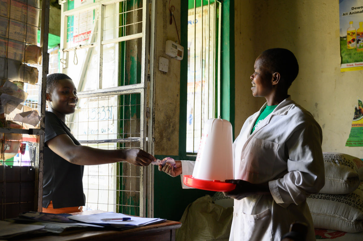 A woman selling a pan and jar poultry water drinker to a customer visiting her agrovet center.