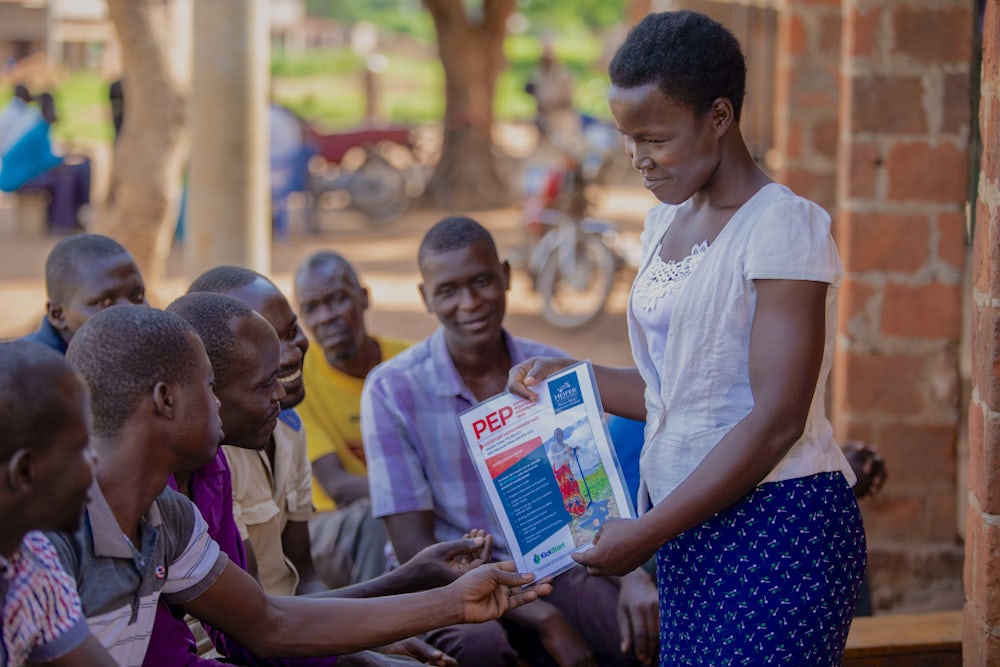 A young woman in Uganda uses a paper flier to teach a small group of youth.