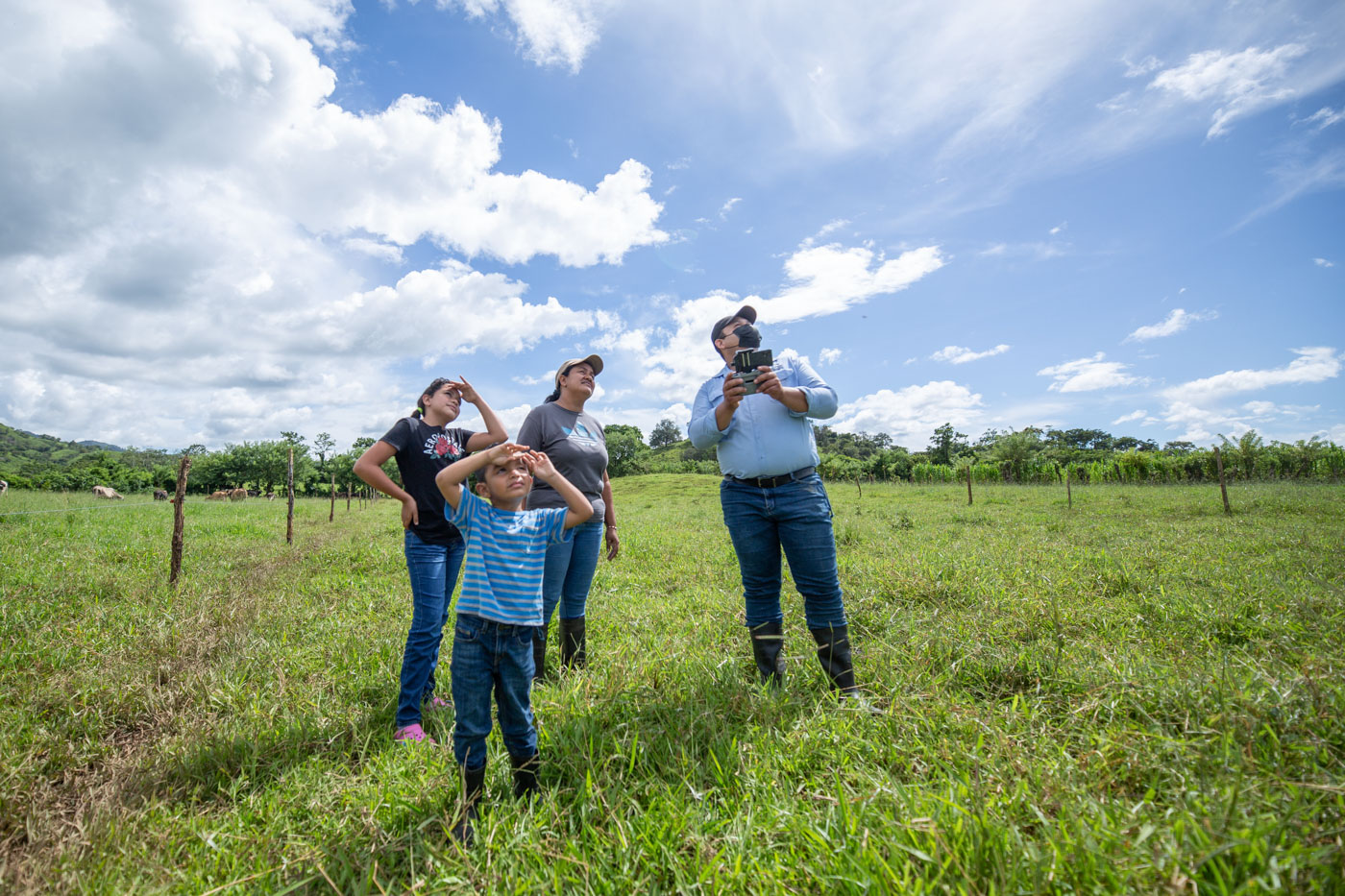 A woman and two children look up as a man flies a drone above them.